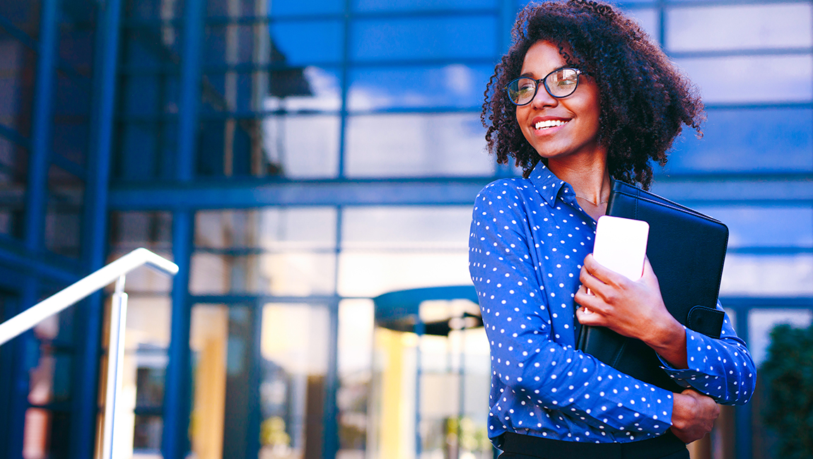 Businesswoman holding phone and smiling outside of an office building